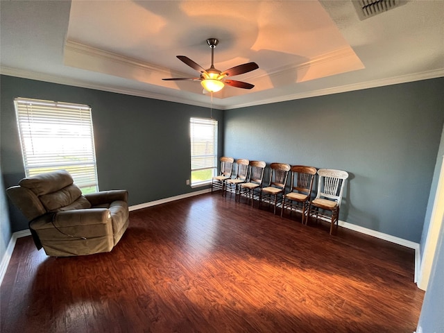 living area with dark hardwood / wood-style floors, ornamental molding, and a tray ceiling