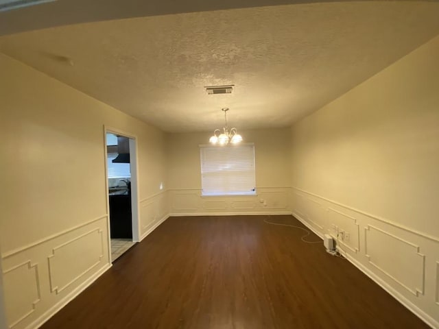 unfurnished dining area featuring a textured ceiling, an inviting chandelier, and dark wood-type flooring