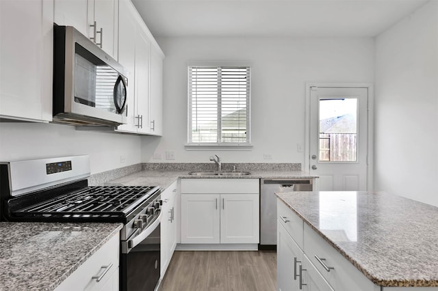 kitchen featuring white cabinets, appliances with stainless steel finishes, light stone counters, and sink