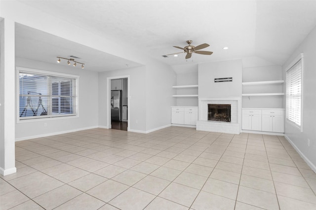 unfurnished living room featuring built in shelves, ceiling fan, a brick fireplace, vaulted ceiling, and light tile patterned floors