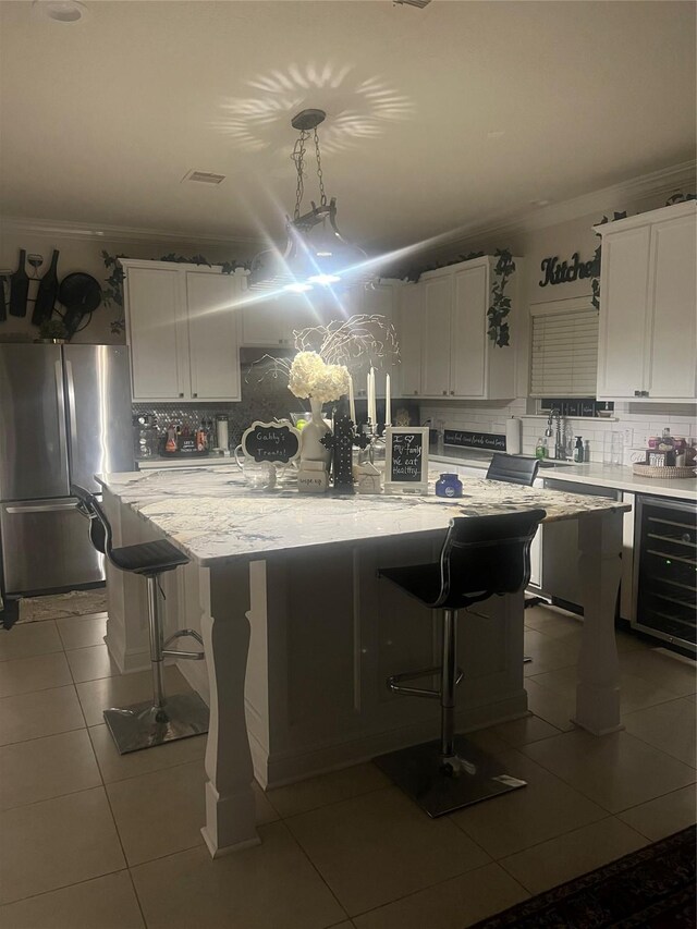 kitchen featuring stainless steel refrigerator, white cabinetry, a center island, pendant lighting, and a kitchen bar