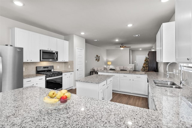 kitchen with light stone countertops, stainless steel appliances, sink, a center island, and white cabinetry