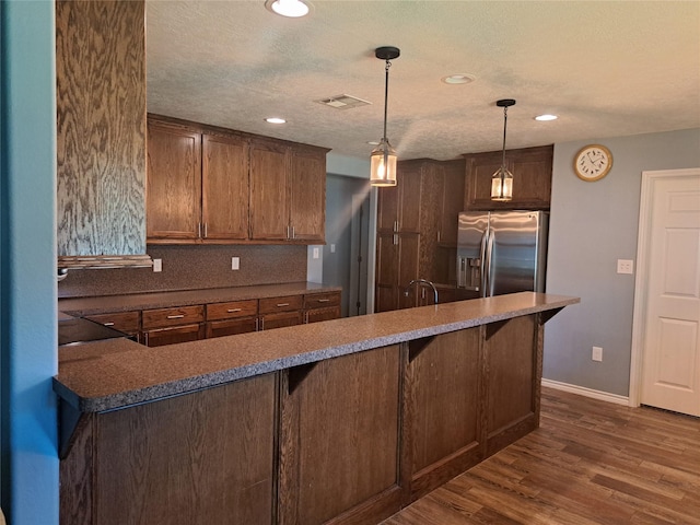 kitchen featuring stainless steel fridge with ice dispenser, dark hardwood / wood-style floors, kitchen peninsula, pendant lighting, and a breakfast bar