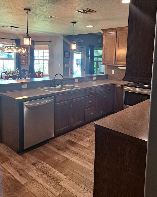 kitchen featuring sink, tasteful backsplash, light hardwood / wood-style floors, a textured ceiling, and appliances with stainless steel finishes