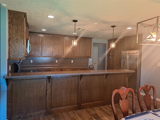 kitchen with a kitchen bar, stainless steel fridge, dark wood-type flooring, decorative light fixtures, and range