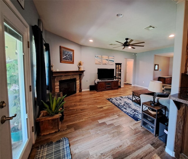 living room with a stone fireplace, ceiling fan, and light hardwood / wood-style flooring