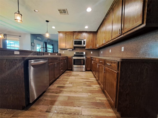 kitchen with sink, decorative light fixtures, light hardwood / wood-style floors, kitchen peninsula, and stainless steel appliances