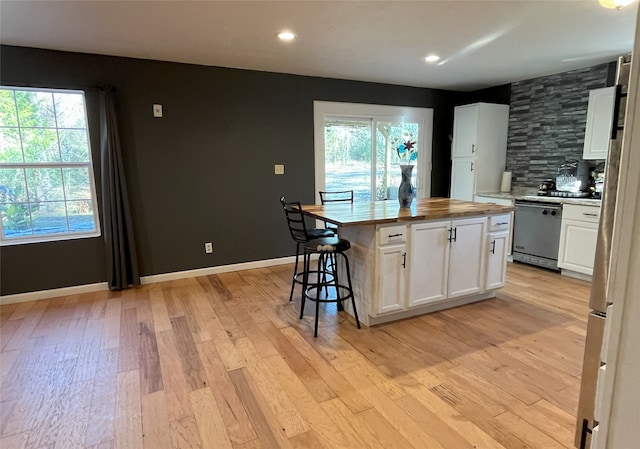 kitchen featuring wooden counters, stainless steel dishwasher, light hardwood / wood-style flooring, a center island, and white cabinetry