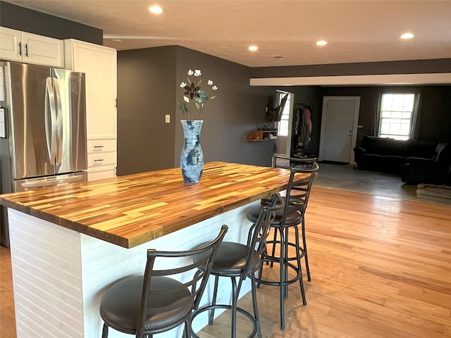 kitchen featuring butcher block countertops, a kitchen island, a kitchen bar, white cabinetry, and stainless steel refrigerator