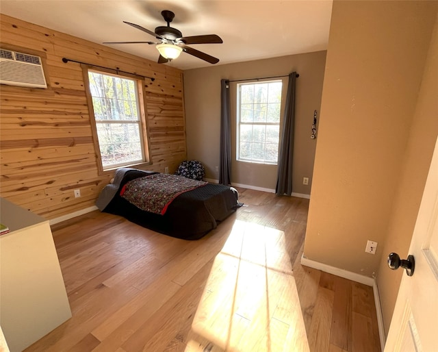 bedroom featuring an AC wall unit, ceiling fan, wooden walls, and light hardwood / wood-style flooring