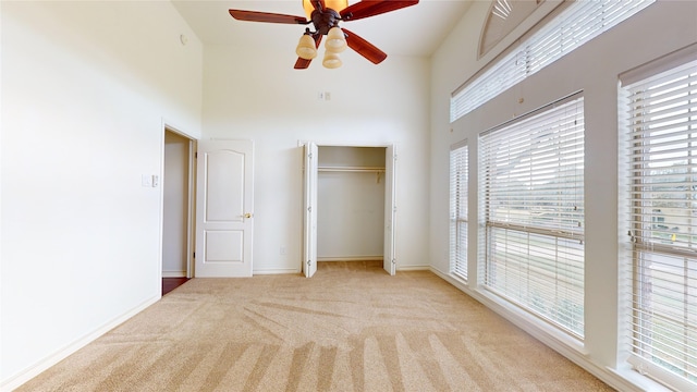 unfurnished bedroom featuring ceiling fan, light colored carpet, and a high ceiling