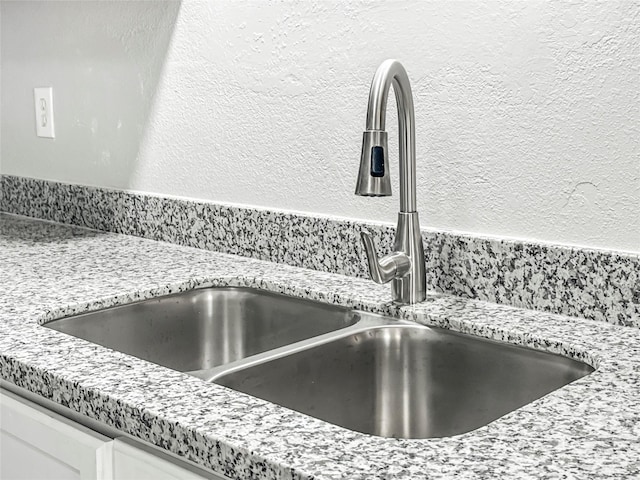 interior details featuring light stone countertops, sink, and white cabinets