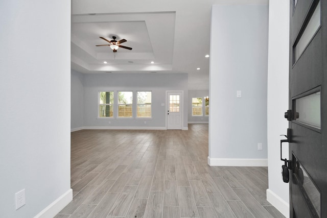 unfurnished living room featuring a tray ceiling, ceiling fan, and light hardwood / wood-style flooring