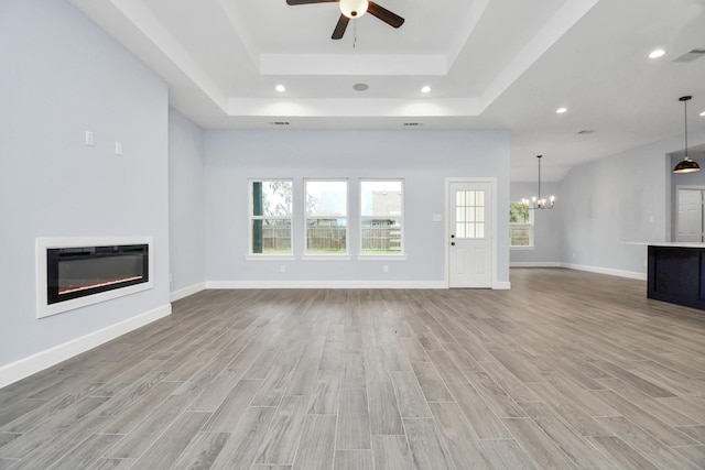 unfurnished living room featuring a raised ceiling, heating unit, light hardwood / wood-style floors, and ceiling fan with notable chandelier