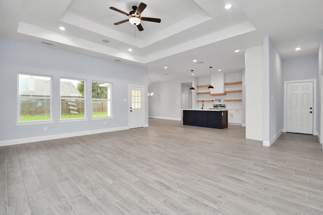 unfurnished living room featuring a raised ceiling, ceiling fan, sink, and light hardwood / wood-style floors