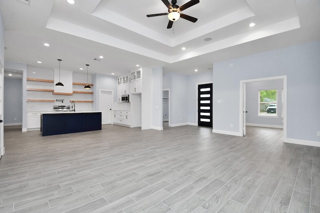 unfurnished living room featuring ceiling fan, light hardwood / wood-style floors, sink, and a tray ceiling