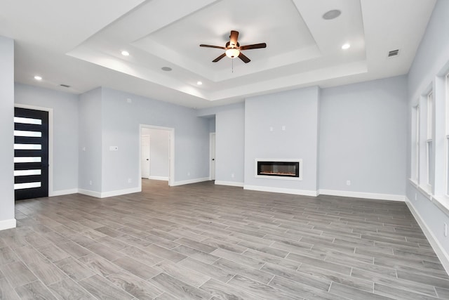 unfurnished living room featuring ceiling fan and a raised ceiling