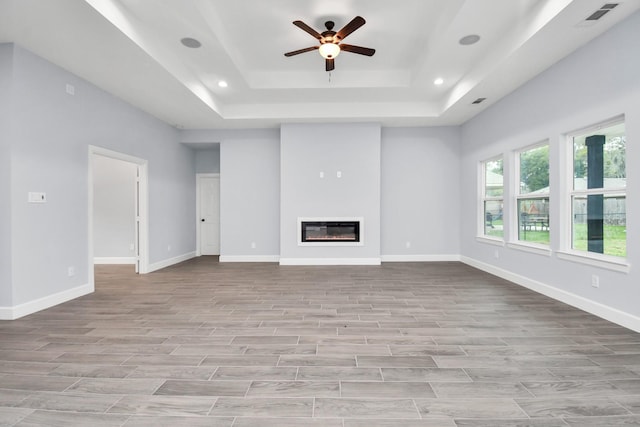 unfurnished living room with ceiling fan and a tray ceiling