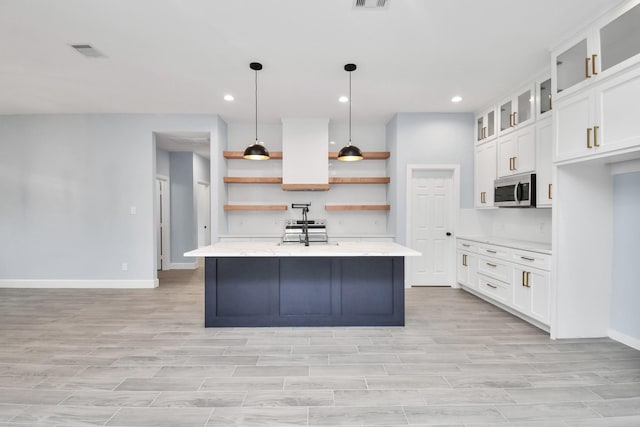 kitchen featuring light stone countertops, appliances with stainless steel finishes, a kitchen island with sink, pendant lighting, and white cabinets