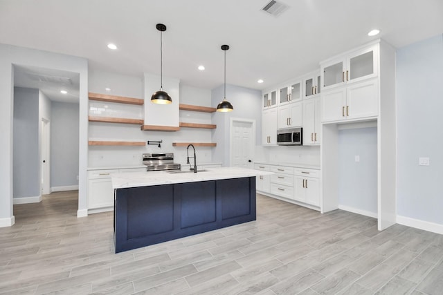 kitchen featuring white cabinets, appliances with stainless steel finishes, light stone countertops, and a kitchen island with sink