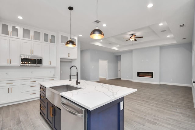 kitchen with a raised ceiling, white cabinetry, stainless steel appliances, and a kitchen island with sink