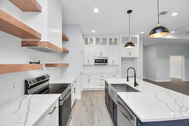 kitchen featuring white cabinets, light stone counters, stainless steel appliances, and an island with sink