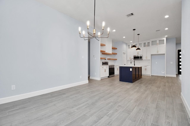 kitchen with a kitchen island with sink, sink, appliances with stainless steel finishes, decorative light fixtures, and white cabinetry