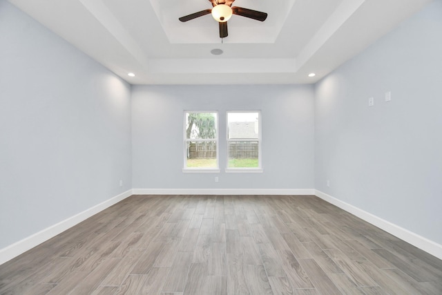 empty room with a raised ceiling, ceiling fan, and light hardwood / wood-style flooring