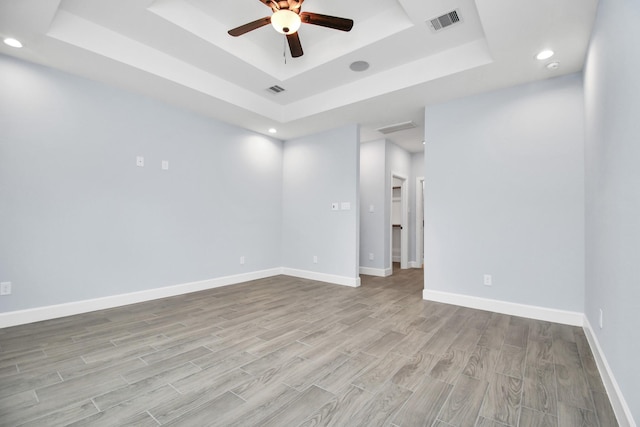 empty room featuring ceiling fan, light hardwood / wood-style floors, and a raised ceiling