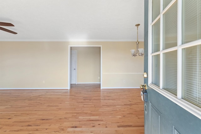 empty room with crown molding, ceiling fan with notable chandelier, and light wood-type flooring