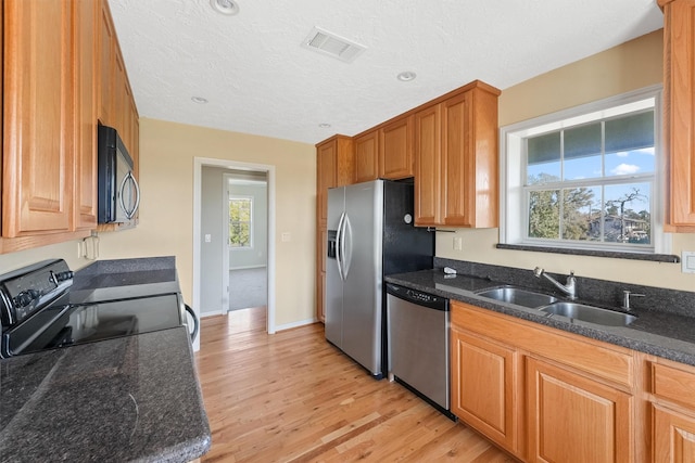 kitchen featuring black appliances, sink, light hardwood / wood-style flooring, dark stone countertops, and a textured ceiling