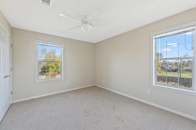 carpeted spare room with ceiling fan, a textured ceiling, and a wealth of natural light