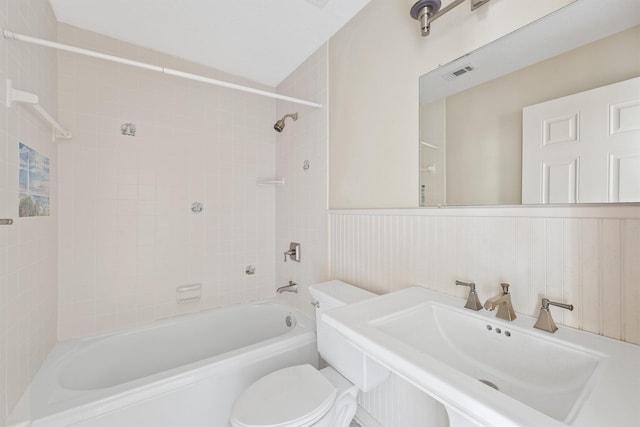 full bathroom with tiled shower / bath combo, wood walls, toilet, and sink