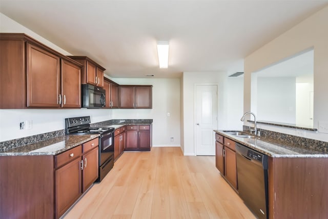 kitchen featuring sink, light hardwood / wood-style flooring, dark stone countertops, and black appliances