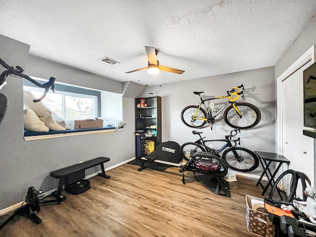 exercise room featuring ceiling fan, wood-type flooring, and a textured ceiling