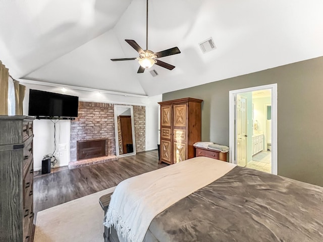 bedroom with vaulted ceiling, a brick fireplace, ceiling fan, dark hardwood / wood-style floors, and connected bathroom