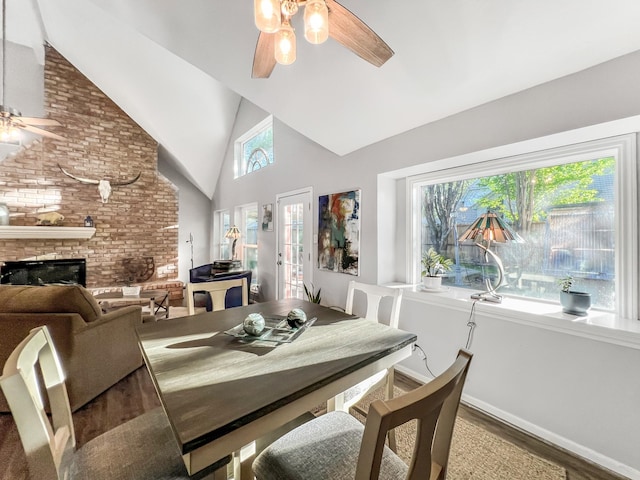 dining area with hardwood / wood-style floors, ceiling fan, high vaulted ceiling, and a brick fireplace