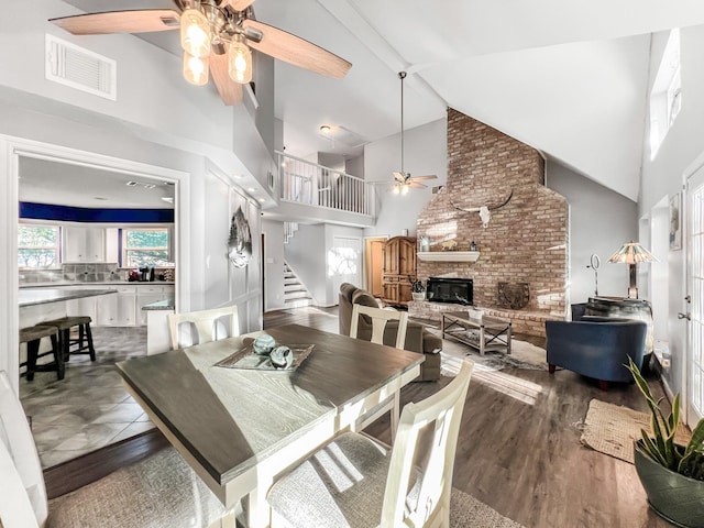 dining room with ceiling fan, a fireplace, high vaulted ceiling, and dark wood-type flooring