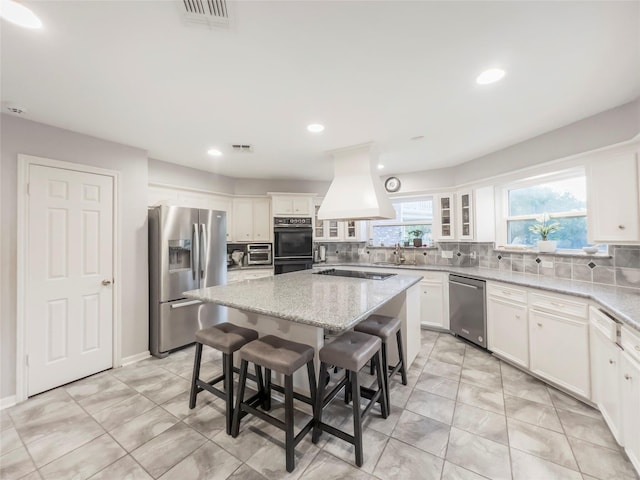 kitchen featuring a center island, light stone counters, a kitchen bar, black appliances, and custom range hood