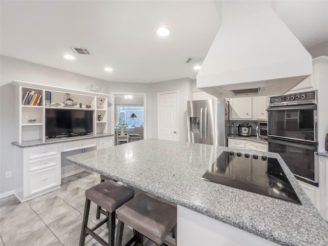 kitchen featuring a kitchen bar, premium range hood, light stone counters, black appliances, and white cabinetry