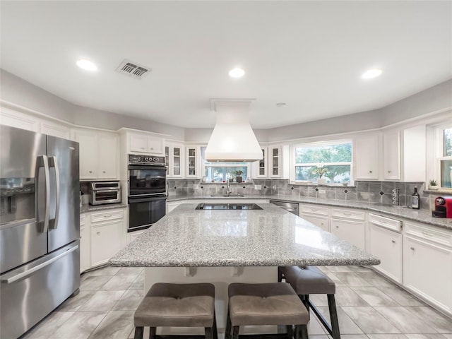 kitchen with black appliances, a center island, white cabinets, and custom range hood