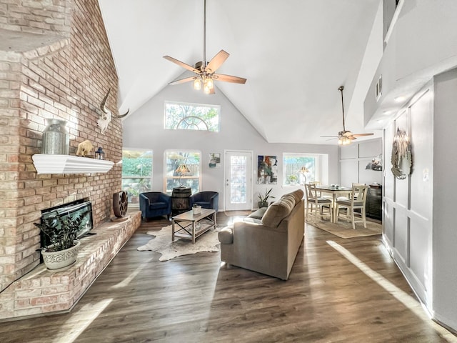 living room featuring ceiling fan, a healthy amount of sunlight, a high ceiling, and a brick fireplace