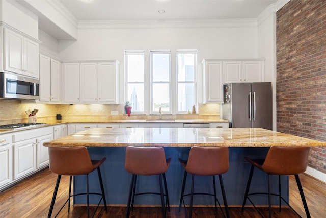 kitchen featuring light stone countertops, stainless steel appliances, hardwood / wood-style flooring, white cabinets, and a center island