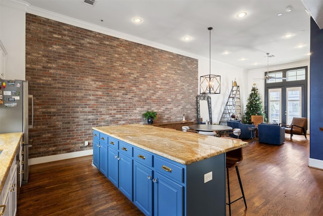 kitchen with light stone counters, brick wall, blue cabinets, a center island, and dark hardwood / wood-style floors