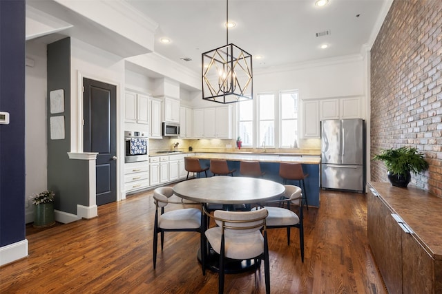 kitchen with stainless steel appliances, brick wall, dark hardwood / wood-style floors, pendant lighting, and white cabinets