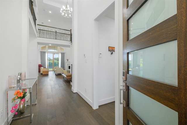 corridor with dark wood-type flooring, a high ceiling, and an inviting chandelier