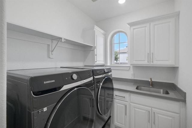 clothes washing area featuring washing machine and dryer, sink, and cabinets