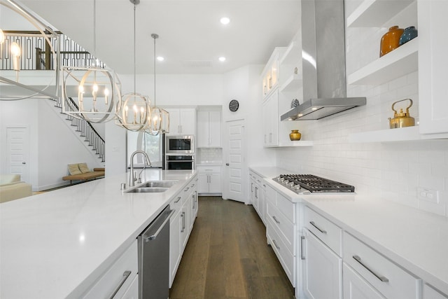 kitchen featuring white cabinetry, sink, stainless steel appliances, wall chimney range hood, and decorative light fixtures