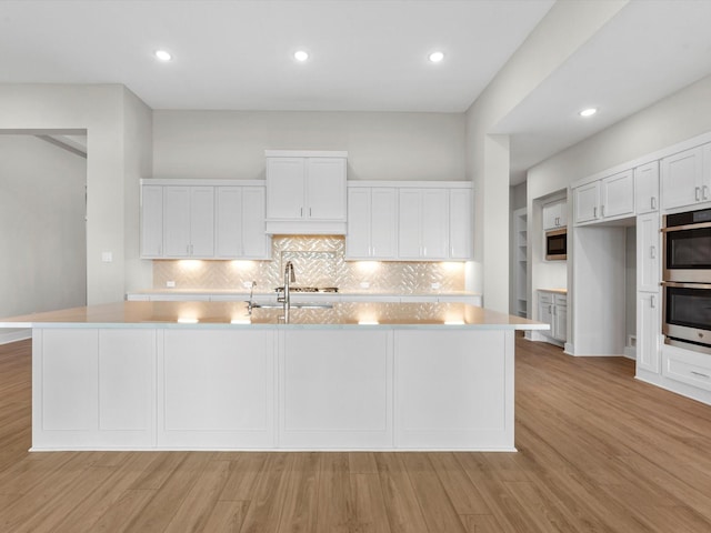 kitchen with a large island, stainless steel double oven, white cabinetry, and light hardwood / wood-style flooring