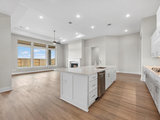 kitchen featuring a tray ceiling, a center island with sink, white cabinets, and stainless steel appliances